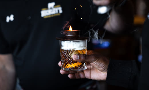 A member of staff holding a smoked cocktail, smoke curling from the glass topper