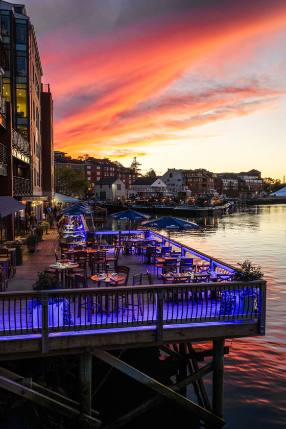 A waterfront restaurant deck lit blue at sunset, the sky burning orange over the water