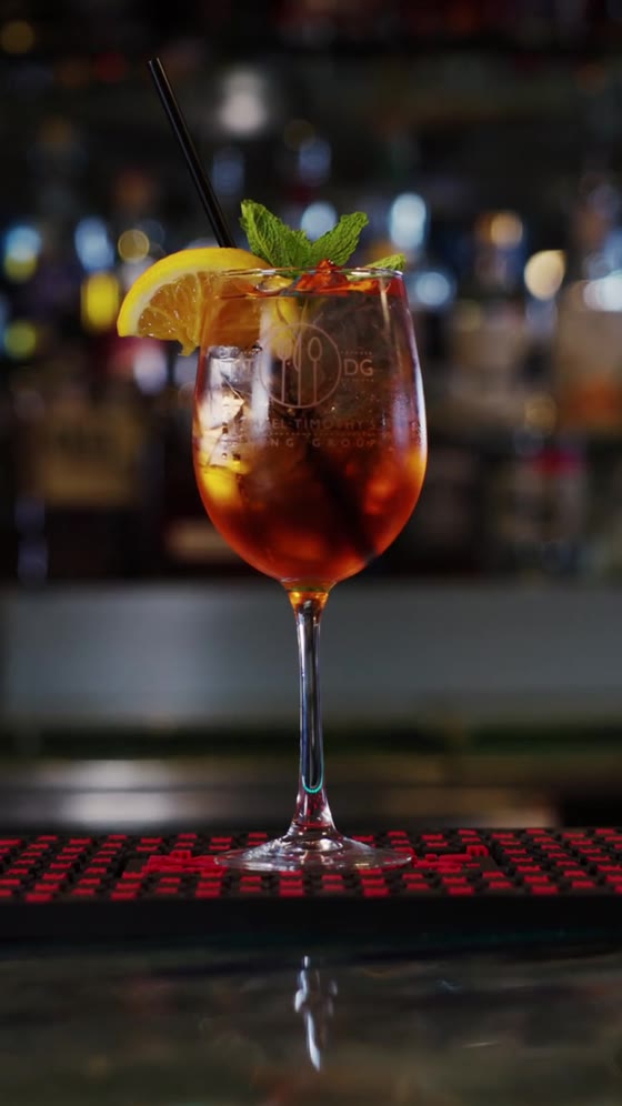 A tall cocktail with a citrus wheel and mint, lit on a dark bar